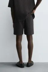 Bermuda de hombre, corte regular fit, color oscuro con patrón de rayas verticales finas en tono marrón claro. Presenta cintura elástica ajustable con cordón interior, bolsillos frontales y un bolsillo trasero de plastrón.