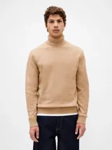 Buzo tipo polera de tejido suave, color beige, con cuello alto, mangas largas y puños y ruedo acanalados.