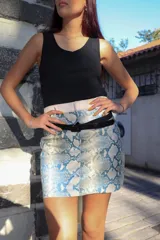 Minifalda con estampado de piel de serpiente en tonos celeste y blanco, con pretina ancha color crudo y cinturón fino negro.