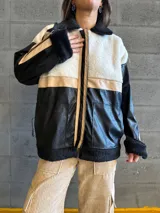 Campera con cuerpo de corderito color beige, mangas y parte inferior de cuero sintético negro con textura tipo cocodrilo. Tiene cuello estilo camisa con solapas de corderito negro, cierre frontal con cremallera y bolsillos laterales.