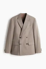 Blazer cruzado de corte relajado, color beige, con solapas de pico, cierre de doble botonadura, bolsillos ribeteados con solapa en la parte frontal y abertura en la parte trasera.