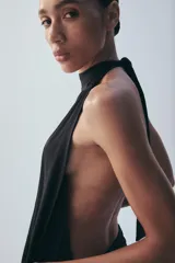 Mono largo negro con cuello halter, hombros descubiertos, parte superior drapeada y piernas anchas con bajo acabado en puño elástico.