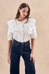 Blusa blanca de algodón con bordado floral, cuello redondo, manga corta con volados y cierre frontal con botones.