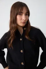 Cardigan de punto negro con cuello camisero, cierre frontal de botones y mangas largas con puños acanalados.