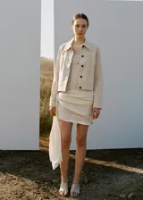 Chaqueta de algodón estilo tejano en color beige, con cuello camisero, manga larga, dos bolsillos de parche en el frente y cierre delantero de botones.