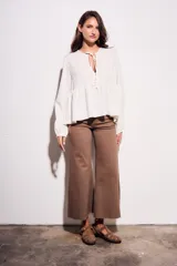 Blusa color crudo de viscosa y lino con bordados en el frente, escote con lazo y mangas largas. Corte holgado con frunce en la cintura.