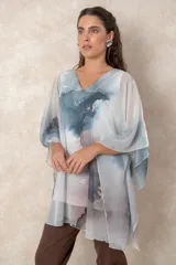 Blusa tipo túnica de gasa semitransparente con escote en V y mangas amplias. Presenta un diseño estampado con efecto acuarela en tonos azules, grises y marrones sobre fondo blanco.