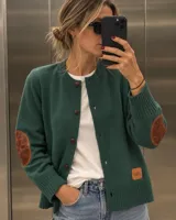 Cardigan de punto color verde oscuro, con cuello redondo, cierre frontal de botones y coderas de cuero marrón. Presenta ribetes en rib y detalle de etiqueta de cuero en el dobladillo.