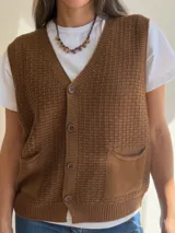 Chaleco de tejido de punto con textura, escote en V y cierre frontal con botones. Presenta dos bolsillos delanteros y terminaciones en tejido acanalado en el ruedo.