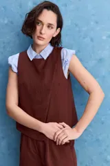 Top blanco sin mangas, con cuello redondo, diseño cruzado en el frente y cierre con botones en el hombro.