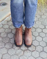 Botinetas de cuero color marrón con diseño combinado en cuero liso y gamuza. Presentan suela track de goma negra con taco cuadrado y tirador en la parte trasera.