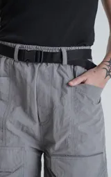 Bermuda cargo color gris oscuro (carbón), de corte recto y largo hasta la rodilla, con cinturón de cinta negra ajustable con hebilla de plástico. Presenta bolsillos laterales y bolsillos cargo con solapa en las piernas.