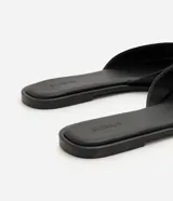 Sandalia mule plana de cuero color negro, con diseño minimalista, capellada ancha y punta cuadrada.