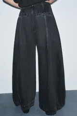 Jeans de tiro alto con diseño de pierna tipo balloon, confeccionados en denim de color gris oscuro con efecto lavado. Presentan costuras verticales marcadas a contraste, bolsillos laterales ocultos y cierre lateral con cremallera.