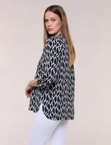 Blusa de calce suelto y caída ligera en color negro con estampado geométrico blanco. Presenta escote en V, cuello mao, abotonadura frontal metálica y bolsillos superiores en el pecho. Cuenta con mangas largas regulables con presilla y botón, ruedo redondeado con tajos laterales y canesú en la espalda.