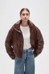 Campera de eco-cuero color marrón con cuello alto, cierre frontal oculto y bolsillos laterales. Presenta un diseño acolchado con acabado brillante.