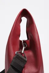 Bolso de mano mediano de piel vacuna, color negro, con estructura blanda y forma de cubo o 'paper bag'. Posee asas de mano cortas y una correa ajustable y extraíble de tela azul marino. El logo de Bimba y Lola está grabado en la parte inferior frontal.