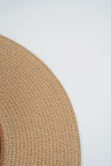 Sombrero de paja tejido color beige, de ala ancha y copa redonda, con cinta decorativa de cuero marrón claro.
