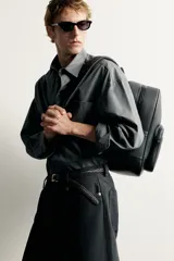 Mochila negra con acabado texturizado y detalle metálico. Cuenta con compartimento principal con cierre de cremallera, bolsillo frontal con cierre, asa de mano superior y correas ajustables para los hombros.