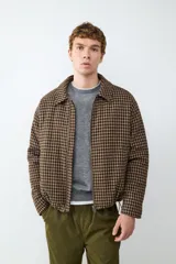 Campera de paño con diseño de cuadros en tonos café y negro, cuello clásico, cierre frontal con cremallera y bolsillos laterales.