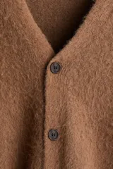 Cárdigan de punto marrón con textura peluda, cuello en V pronunciado y cierre frontal de botones. Presenta remates acanalados en puños y bajo, con un corte holgado.