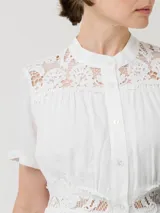 Vestido midi de lino orgánico y viscosa en color blanco, con cuello mao, mangas cortas y cierre frontal con botones. Presenta detalles de encaje en los hombros, el pecho y la cintura, además de forro interior a tono.