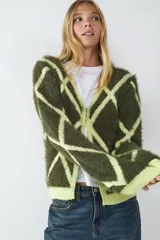 Cardigan de punto con cuello en V, manga larga y cierre frontal de botones. Presenta un estampado geométrico de rombos en contraste, con base verde oliva y líneas en verde lima. El tejido es de punto peluche.