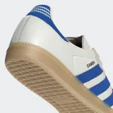 Championes Adidas Samba OG de diseño clásico, con parte superior de cuero blanco, superposiciones de gamuza gris claro en la puntera y el área de los cordones, y las icónicas tres rayas en azul vibrante. Presenta un detalle de tejido acanalado azul en el talón y suela de goma color caramelo.