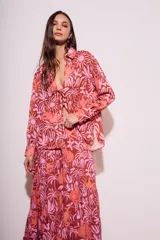 Blusa de poliéster con estampado de flores y animales en tonos rosa y marrón. Tiene cuello camisero, mangas largas y cierre frontal con lazo.