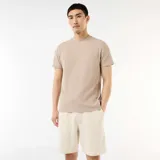 Camiseta de cuello redondo y manga corta color beige, con textura de nido de abeja y pequeña etiqueta decorativa en el borde inferior.
