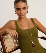 Conjunto de bisutería compuesto por un collar largo con cadena dorada y dije en forma de gota con detalle de resina, y un par de aros tipo argolla gruesa con baño en tono dorado.