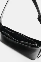 Bolso de hombro de diseño asimétrico en color negro, con acabado brillante de charol, asa ajustable y cierre de cremallera.