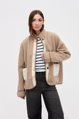 Campera de sherpa doble faz en color crema con detalles en verde oliva. Presenta cierre frontal con botones, bolsillos laterales de nylon capitoneado y terminaciones en contratono. Diseño de calce relajado con bordado en la manga.