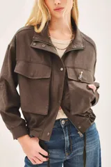 Campera de corte amplio, color marrón, con cierre frontal, bolsillos frontales con solapa y cintura ajustable. Incluye un pin decorativo en la solapa.