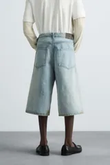 Bermudas de denim de algodón, color celeste claro con efecto lavado y manchas marrones/beige en las perneras. Tienen un corte ancho (baggy fit) y terminación de bajo irregular.