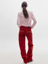 Pantalón de pana roja con corte holgado y tiro medio. Presenta una línea dorada a lo largo de la pierna.
