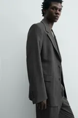 Blazer de corte regular fit en color gris oscuro, confeccionada en tejido con viscosa. Presenta cuello con solapas de muesca, cierre frontal con dos botones, bolsillos laterales con solapa y aberturas en la espalda.