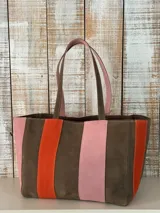 Cartera de cuero tipo shopper de diseño amplio, con diseño de franjas verticales en tonos marrón, naranja y rosado, doble asa de hombro y cierre superior.