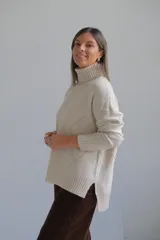Polerón de cuello alto con diseño de rombos tejidos en relieve, mangas largas con puños acanalados y ruedo asimétrico con aberturas laterales.
