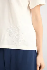 Remera azul marino de manga corta, corte recto y cuello redondo, con detalle de aplicación bordada de flores de crochet en el lateral inferior.