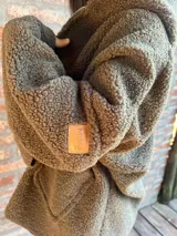 Campera de corderito color verde oscuro, con diseño holgado, cuello alto y manga larga. Presenta una etiqueta de cuero sintético en la manga.