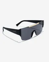 Lentes de sol Hawkers unisex, modelo Paula Echevarría Rubin, con montura negra y lente espejada gris con detalle dorado en la parte superior.