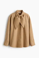 Camisa de corte relajado en tejido dobby con estampado de cuadros, cuello con detalle de moña y botonadura frontal. Presenta hombros caídos y mangas largas con puños abotonados.