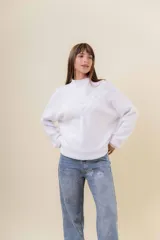 Sweater tejido de punto color blanco, con cuello alto y diseño en relieve tipo chevron en la parte frontal. Presenta un calce holgado con terminaciones acanaladas en puños y ruedo.