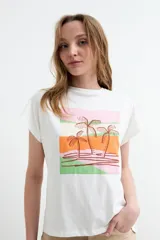 Remera de manga corta color blanco, confeccionada en 100% algodón, con cuello redondo y diseño gráfico frontal estilo paisaje tropical con palmeras en tonos rosado, naranja y verde.