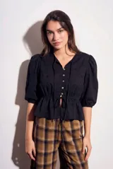 Blusa negra de algodón con diseño de broderie, mangas tres cuartos abullonadas, cierre frontal con botones y detalle de cordón ajustable en la cintura.