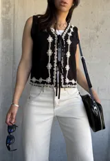 Chaleco negro con bordado de flores blancas, escote en V y lazos de ajuste en el frente.