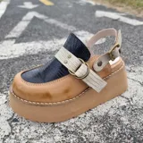 Zueco de cuero color marrón claro, con capellada en cuero negro con textura croco, tiras cruzadas frontales en cuero texturizado claro con hebilla metálica circular y tira ajustable en el talón. Cuenta con suela de plataforma corrida.
