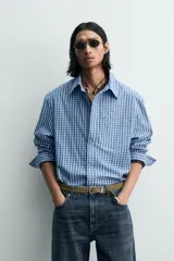 Camisa de manga larga con cuello solapa y bolsillo plastrón en el pecho. Presenta un estampado de cuadros pequeños en tonos azul y blanco. Cierre frontal con botones a presión.