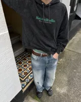 Canguro negro con capucha, de corte regular y confección en felpa suave, con estampa en la espalda de un personaje gráfico y texto "Kaboa Radio".